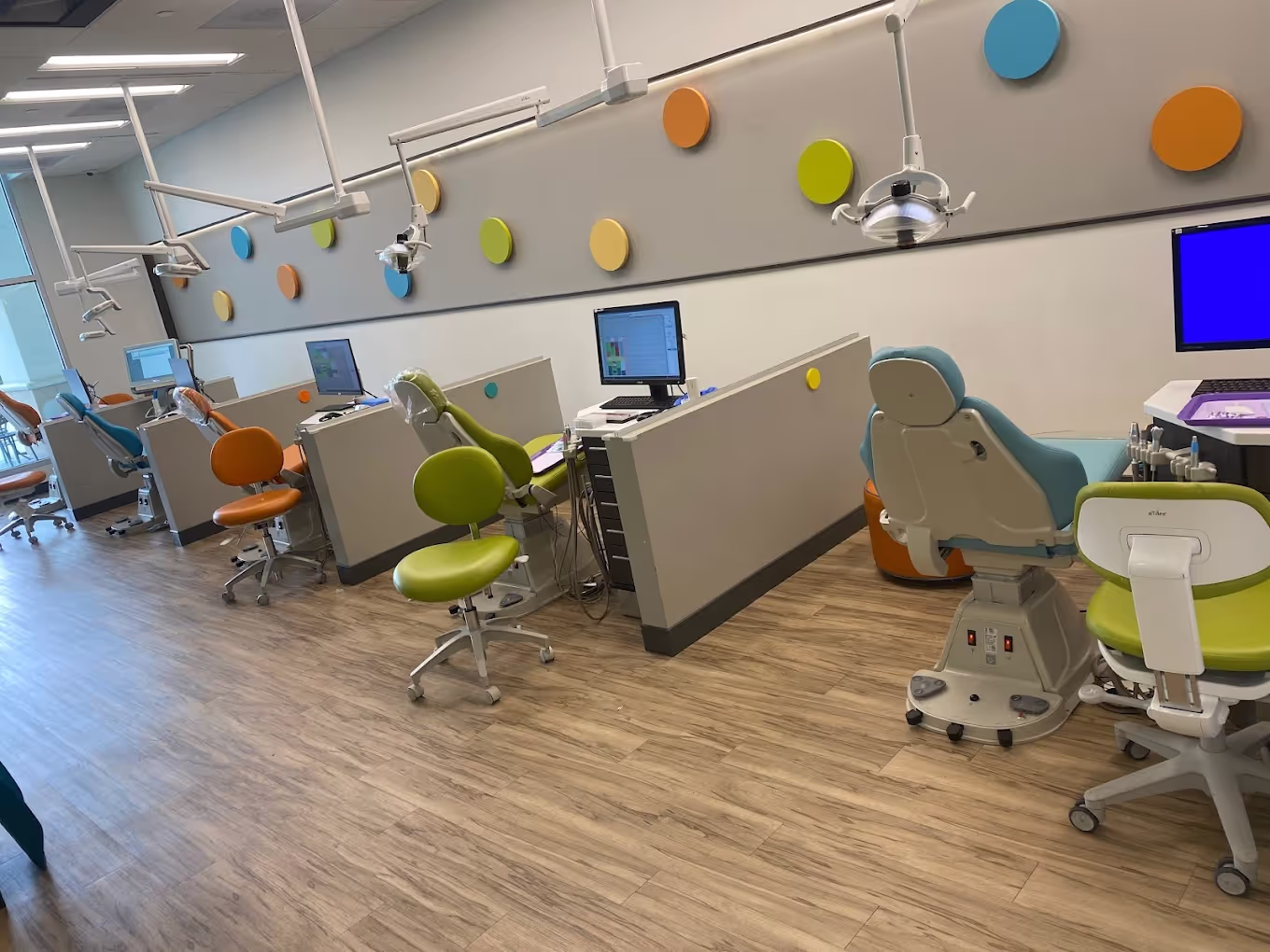 Modern dental clinic with colorful patient and dentist chairs, dental equipment, and computer monitors.