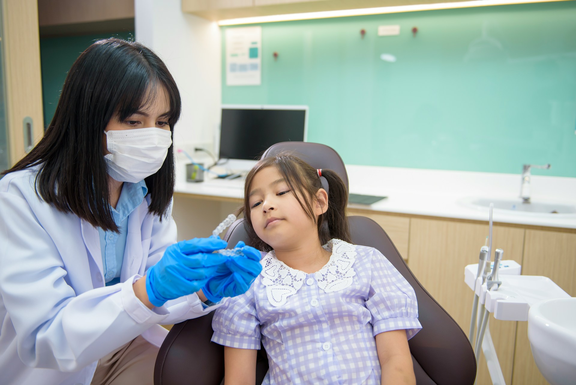 Dentist showing a clear dental aligner to a girl sitting in the dental chair.