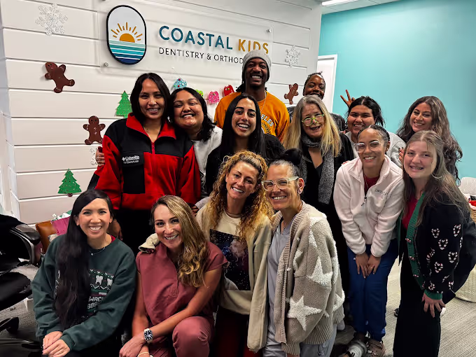 Group of smiling diverse adults posing together inside Coastal Kids Dentistry & Orthodontics office decorated with holiday cutouts.
