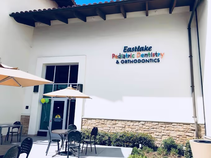 Outdoor seating area with tables, chairs, and umbrellas in front of Eastlake Pediatric Dentistry & Orthodontics building.