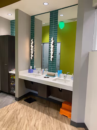 Modern bathroom sink area with a large mirror, turquoise tile accent, hanging string lights, and wooden floor.