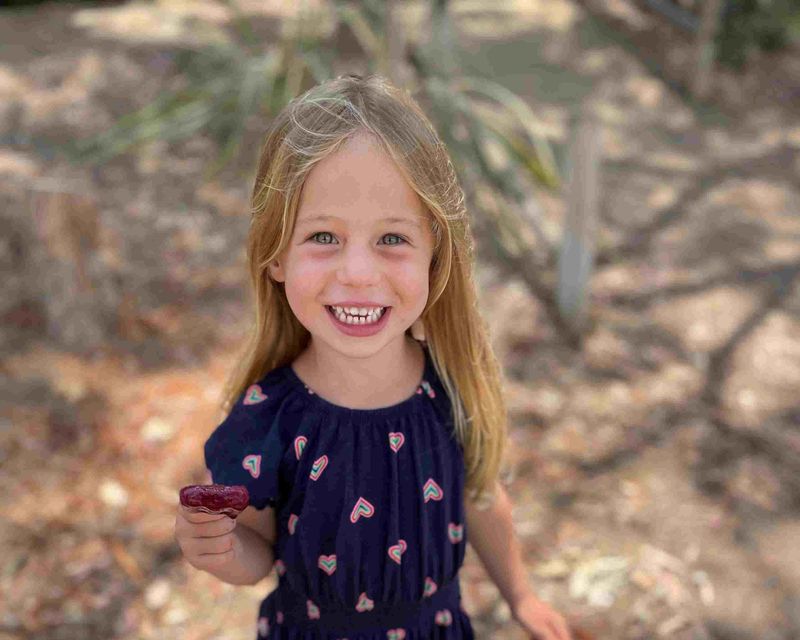 A young Coastal Kids patient grinning ear to ear outdoors in her navy heart-print dress.