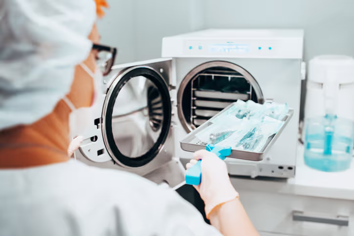 Healthcare worker placing sterilized surgical instruments in an autoclave sterilizer.