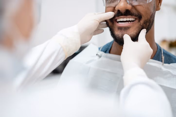 Dentist wearing gloves examining a male patient's teeth during a dental checkup.