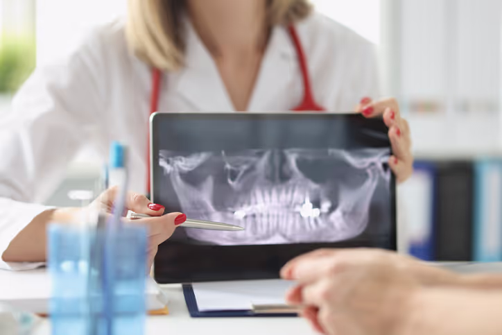 Dentist showing a dental X-ray image of a jaw with teeth and a filling to a patient.