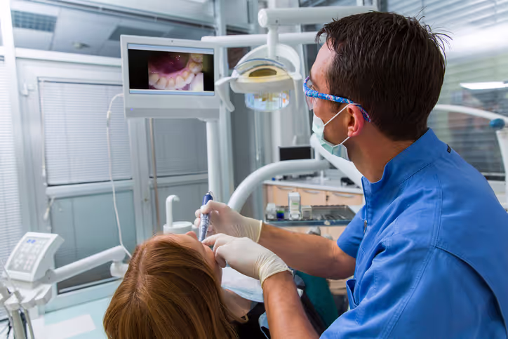 Dentist using an intraoral camera to examine a patient's teeth while viewing the live image on a monitor.