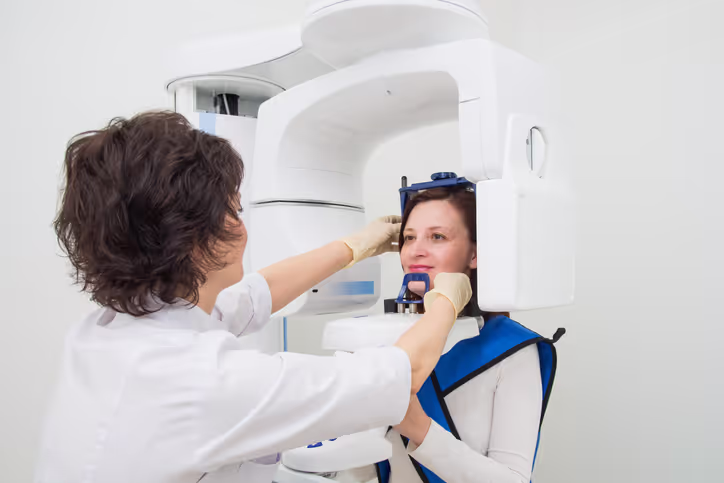 Dental technician adjusting a woman’s head positioning for a panoramic dental X-ray machine.