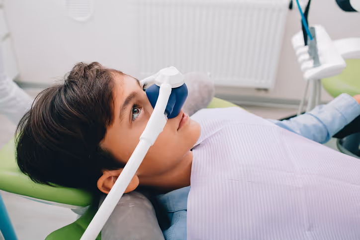 Boy lying in dental chair wearing a sedation mask during dental treatment.