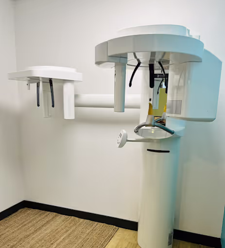 Dental panoramic X-ray machine in a brightly lit room with beige flooring and white walls.