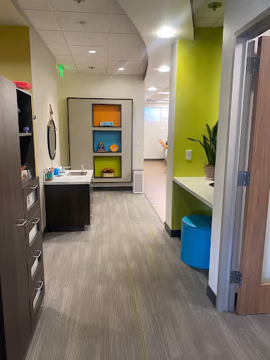 Modern hallway with green walls, a blue stool, a plant on a counter, and shelves displaying decorative items.