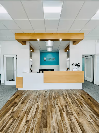 Modern reception desk with light wood accents and blue wall featuring a logo in a bright office space with wood flooring.