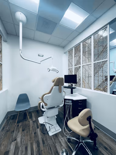 Modern dental examination room with dental chair, dentist stool, computer, and large window with decorative screen.