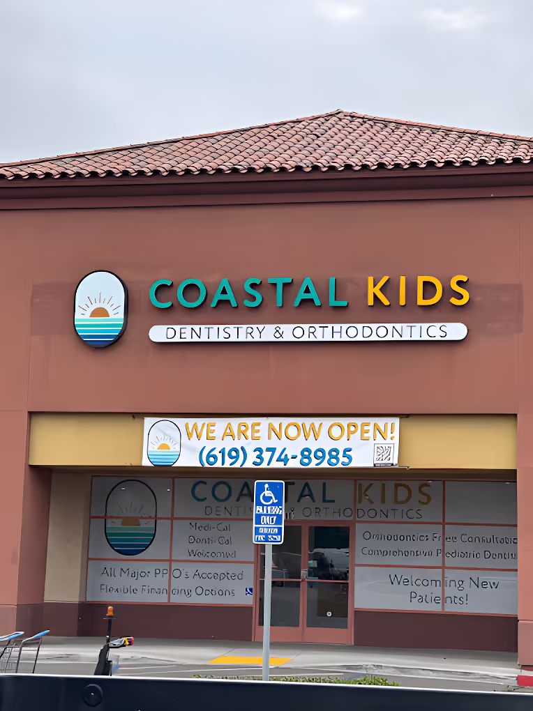 Coastal Kids Dentistry & Orthodontics clinic exterior with a sign announcing it is now open and a visible phone number on the building.