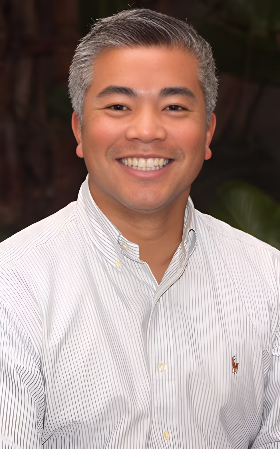 Smiling man with short gray hair wearing a light gray striped button-up shirt.